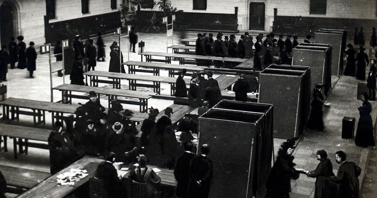 Stemmebokse og borgere i kø til at stemme i rådhushallen 1909.