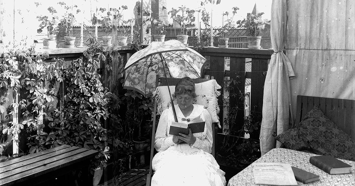 Foto af kvinde, der læser under en parasol på altanen