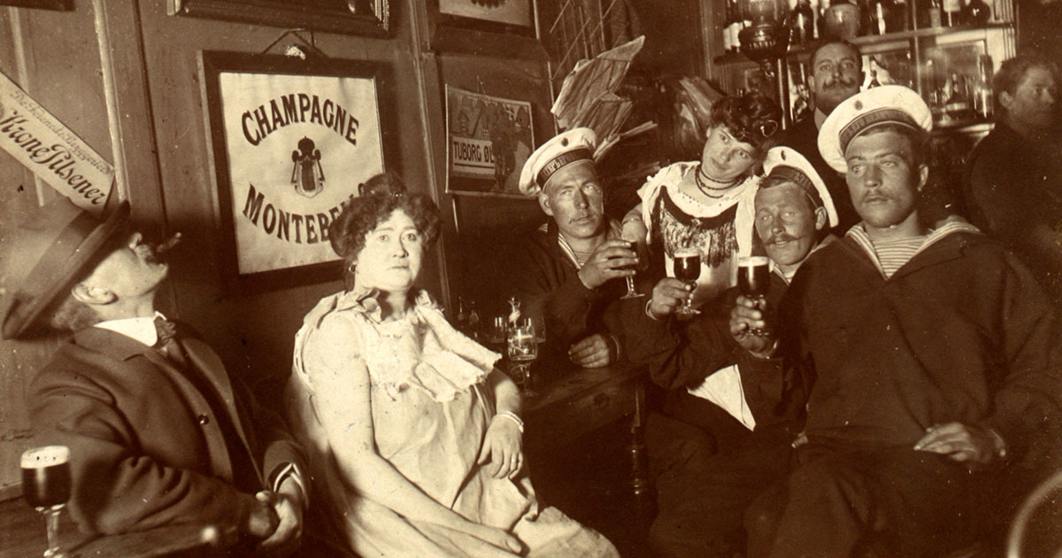 Russiske sømand med løftet glas, en herre med hat og cigar, samt to kvinder.