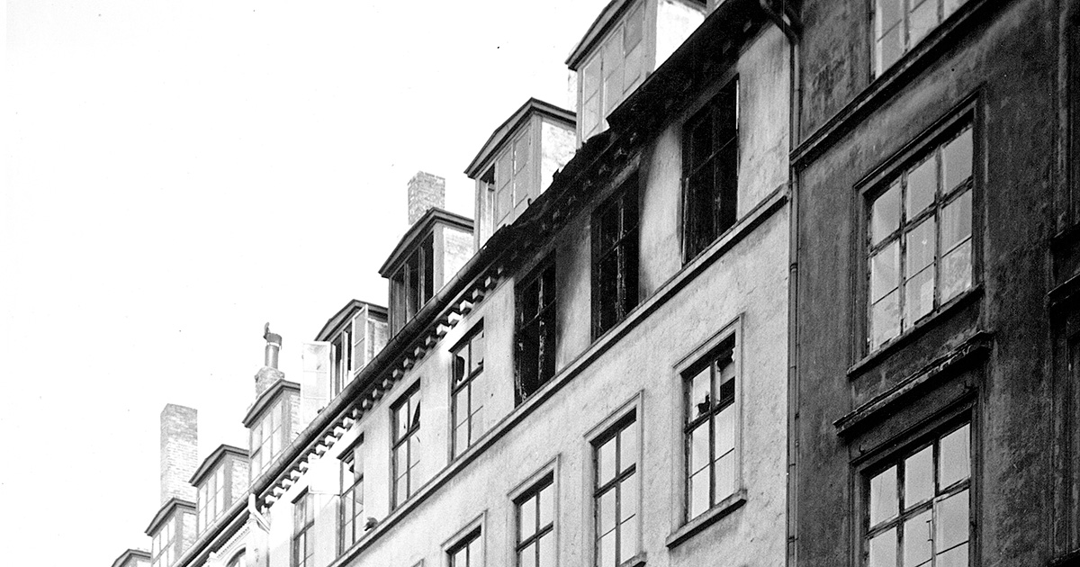 Udsnit af den øverste del af lejlighedsfacade med tre tilsodede vinduer.